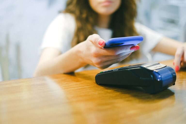 Kobieta płaci smartfonem zbliżeniowo przy terminalu płat